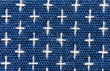 Close-up of machine embroidery sashiko with white crosses on blue background. Textile backdrop made of weaving natural cotton threads. Basis for sewing comfortable clothes, shirts, blouses. Macro