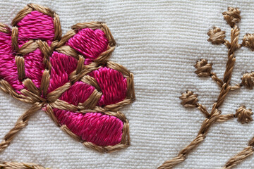 Close-up of a satin stitch embroidery of a floral ornament on a cotton tablecloth. Needlework and...