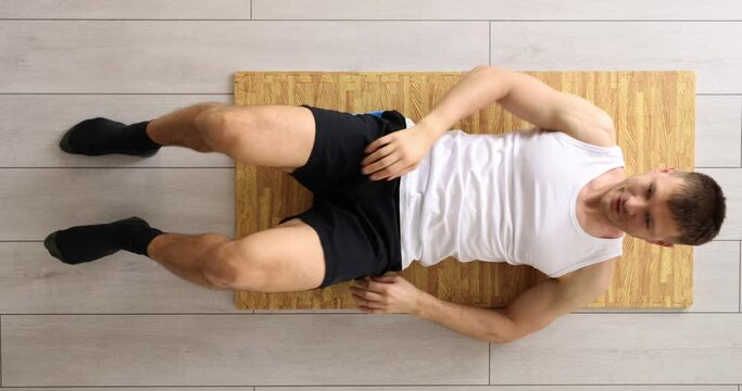 Sports man pumps up muscles of press lying on floor top view. Home fitness workout