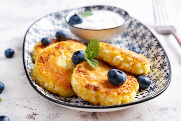 Cottage cheese pancakes with sour cream and blueberries on a light background. Breakfast or lunch