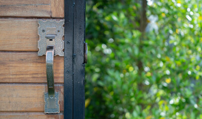 Close up detail shot of a wooden door with ornate handle with nature background.