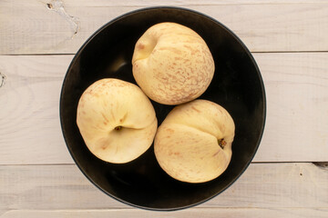Three organic ripe peaches with black ceramic plate on wooden table, macro, top view.