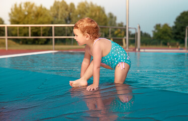 Naklejka premium Little girl is playing in the pool. Happy child outside in the water. Pretty girl in a blue bathing suit. 