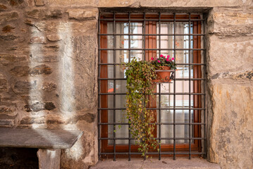 Antica finestra con grata e vaso di fiori in storico paese italiano.