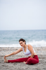 Fototapeta na wymiar Beautiful lady in sportswear stretching on the beach looking at camera