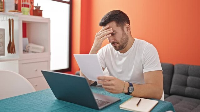 Young hispanic man stressed studying throwing crumpled paper at dinning room
