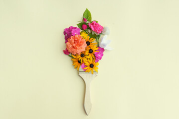 Brush with different colorful flowers on beige background, top view. Creative concept.