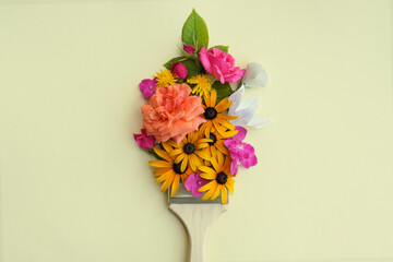Brush with different colorful flowers on beige background, top view. Creative concept.