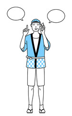 電話をしながら指さしをする夏祭りの法被を着たシニア男性