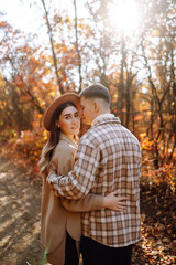 Happy and young couple walks in a beautiful autumn park, enjoys the beautiful weather. Pregnant married couple resting together in nature. Vacation, lifestyle concept.