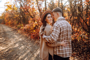 Fototapeta premium Happy and young couple walks in a beautiful autumn park, enjoys the beautiful weather. Pregnant married couple resting together in nature. Vacation, lifestyle concept.
