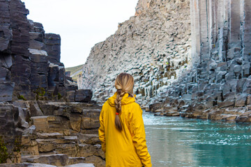 Hiker woman in yellow jacket visiting Studlagil Canyon, Iceland. Famous touristic landmark...
