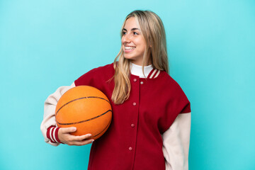 Young caucasian basketball player woman isolated on blue background looking to the side and smiling