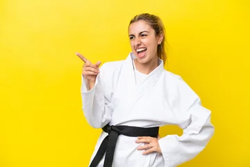Fotobehang Young caucasian woman doing karate isolated on yellow background pointing finger to the side and presenting a product © luismolinero