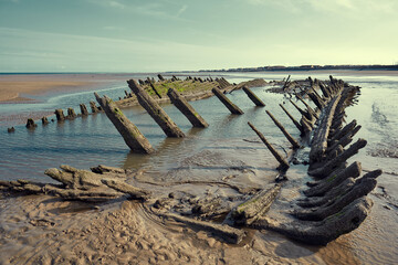 An old historic wooden shipwreck vessel carcass exposed on a desolate tropical island beach. Maritime and exploration disaster. Pirate boats from historical days. Beached ship wrecks