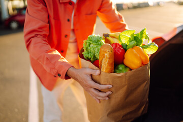 Young man with a bag full of groceries, in a car. Grocery delivery man prepares fresh vegetable delivery service. Healthy lifestyle.