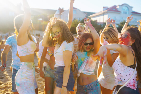 Cheerful young friends with colorful paint on clothes and bodies have fun together at holi festival. Beach party. Friendship, rest, holidays.