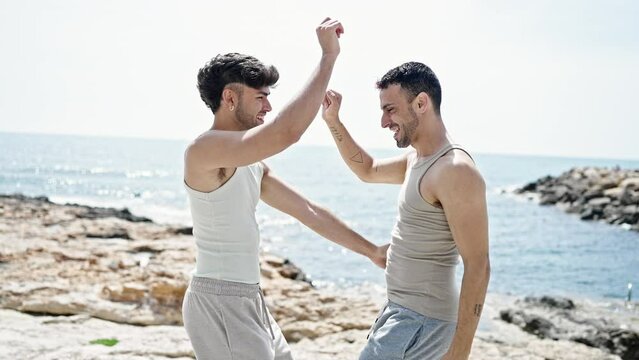 Two men couple smiling confident dancing at seaside