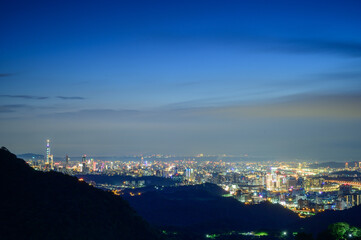 Beautiful city night view with bright lights under blue sky. View of the urban landscape from Dajianshan Mountain, New Taipei City.