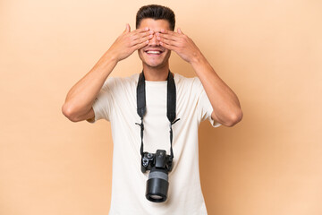 Young photographer caucasian man isolated on beige background covering eyes by hands