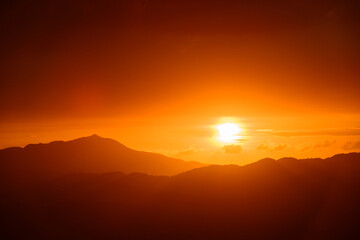 The orange-red sunset is covered by clouds as it moves towards the horizon. View of the urban landscape from Dajianshan Mountain, New Taipei City.