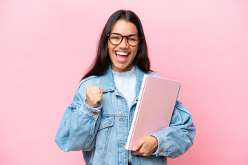Young student Colombian woman isolated on pink background celebrating a victory in winner position