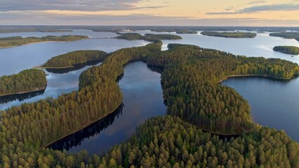Flying over lakeland in Finland. Aerial shot of many green islands at sunset - classical Finnish landscape. Finnish Lake land in sunset lights. Green islands and lake with clouds reflection. 4K, UHD - 628454245