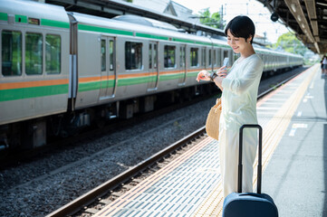 Young Asian woman tourists with a smartwatch cheerfully wait for the train at the station....