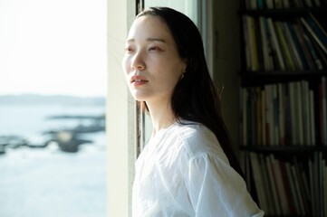 A black-haired woman looking at the scenery from a window overlooking the sea