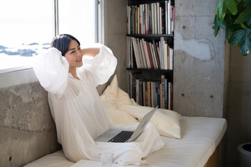 Asian woman sitting relaxed on sofa bed in the room and working using laptop