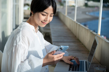 A short-haired woman using a smartphone on the terrace of cafe along the coast