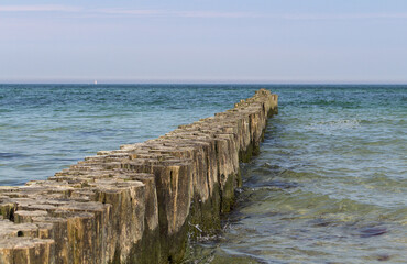 Fototapeta na wymiar Wooden breakwater in the blue turquoise Baltic Sea with horizon and calm water. Diagonal.