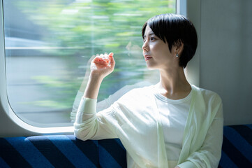 An Asian woman sits on a train seat and looks out the window. Travelling on public transportation