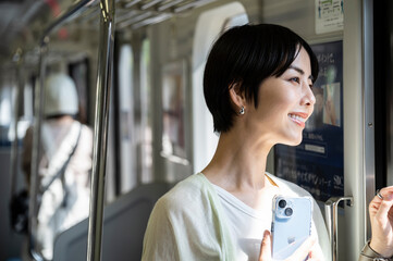 A young Asian woman riding a train with a smartphone.  Travelling on public transportation