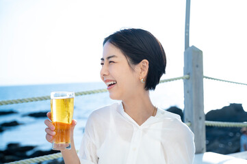 Beautiful Asian woman happily drinking beer at a seaside bar.
