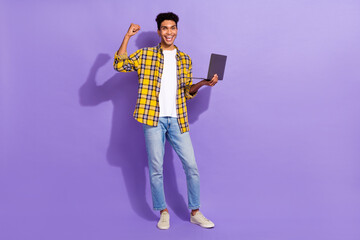Full body photo of delighted cheerful man raise fist use wireless netbook empty space isolated on violet color background