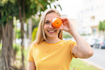 Young blonde woman at outdoors holding an orange