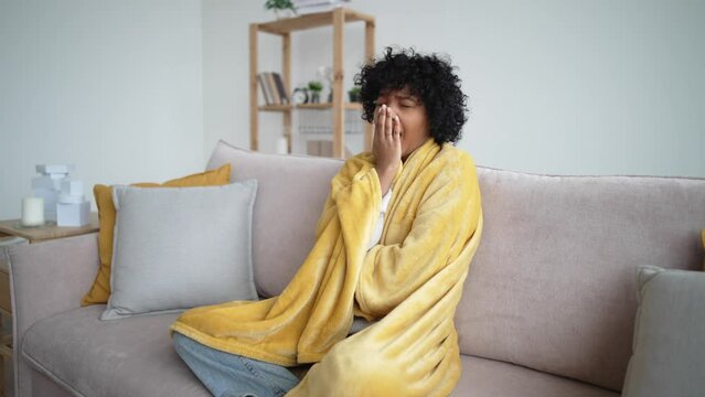 Girl suffering from weakness, high temperature. Sick ill tired african american woman has cold sits on couch at home wrapped in blanket. Flu, influenza, virus, respiratory infection symptoms concept.