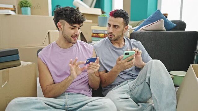Two men couple shopping with smartphone and credit card at new home