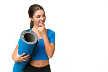 Teenager caucasian girl going to yoga classes while holding a mat over isolated background thinking an idea and looking side