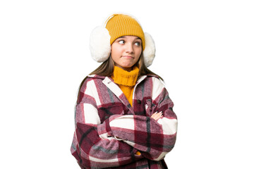 Teenager caucasian girl wearing winter muffs over isolated background making doubts gesture while lifting the shoulders