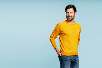 Fototapeta premium Portrait of handsome smiling bearded man wearing autumn yellow sweater, stylish jeans isolated on blue background. Portrait of successful middle aged fashion model posing for pictures, studio shot