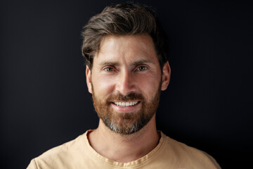 Fototapeta premium Closeup portrait of handsome smiling latin man looking at camera isolated on black background. Happy bearded hipster after barbershop service
