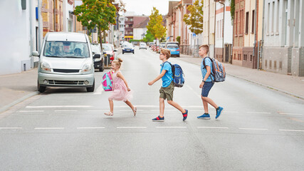 Children cross the street with rucksacks near school. Traffic rules learning at school concept....