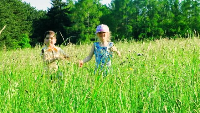 A Little Boy And A Girl Of Primary School Age Run In The Tall Grass. The Concept Of Children's Friendship And Happy Childhood.