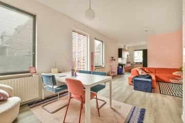 a living room with pink and blue chairs, an orange couch, and a white table in front of the window