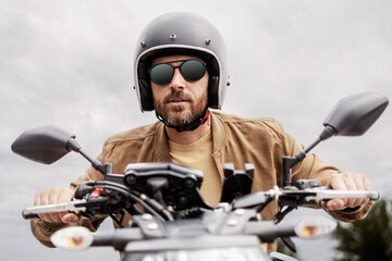 Handsome bearded brutal biker wearing helmet and stylish sunglasses riding motorbike on the road....