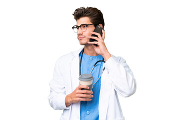 Young doctor man over isolated background holding coffee to take away and a mobile
