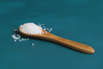 Coarse salt crystals on a blue table. Wooden spoon with sea salt. Background for advertising salty.
