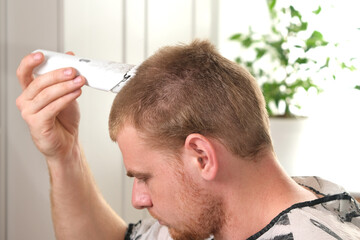 Obraz premium A man cuts his hair with a clipper. Haircut at home. Saving money. Barber shop at home. Change yourself. Lifestyle.